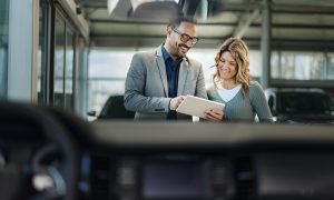 Happy car salesman and his female customer looking at buying plans on digital tablet in a showroom.